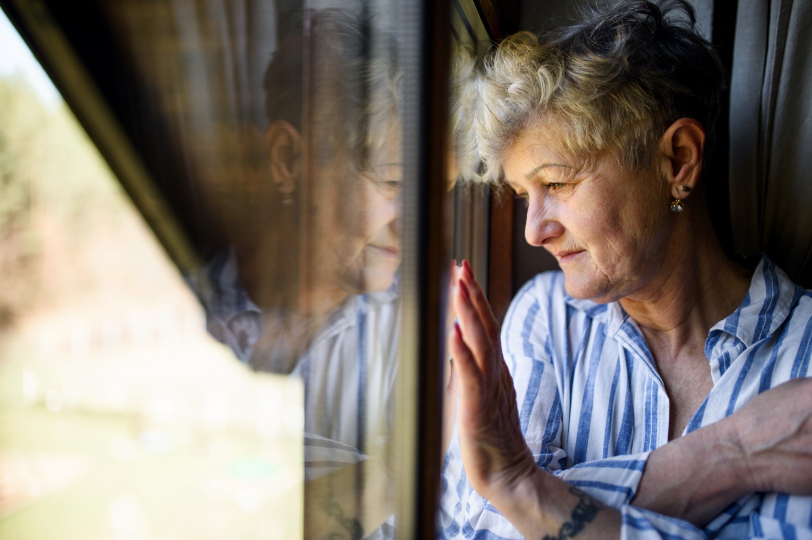 Sad senior woman standing indoors by window at home